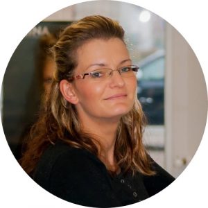 Monika Schwichtenberg steht am Friseurstuhl und schaut seitlich in die Kamera. Sie hat Blondes Haar was über die Schulter reicht.