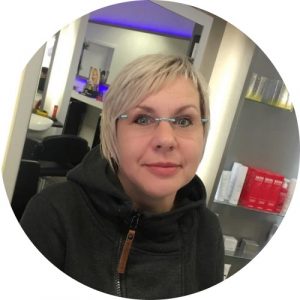 Salonleiterin Susanne Rehberg sitzt am Kosmetikplatz im Salon und schaut sehr freundlich. Sie trägt blonde Haare die bis über die Ohren gehen