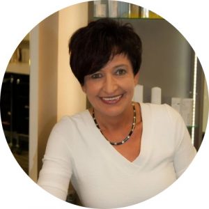 Eine Frau sitzt auf den Kosmetikstuhl und lacht freundlich in die kamera. sie trägt ein weißes oberteil, hat kurze rötliche haare