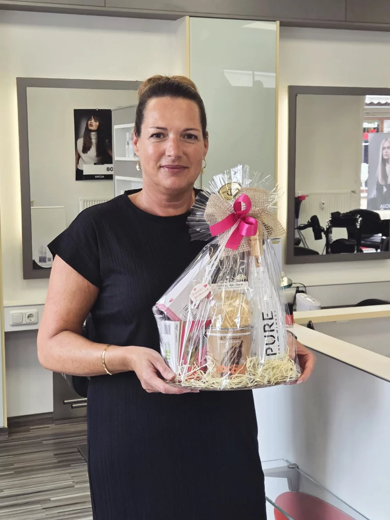 eine Friseurin steht im Salon von Figaro Malchin und hält einen Presentkorb in der Hand.