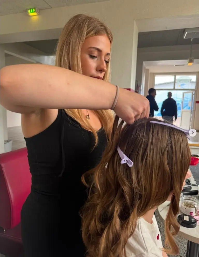 unsere Auszubildene Anne-Marie steht hinter einem Kind aus der Schule und macht dem Kind locken.